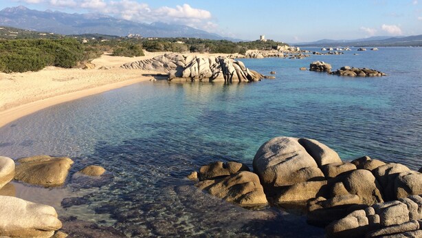A coastal landscape with clear waters, rocky formations, and a distant castle on a hill. - VILLA Sea View with beautiful swimming pool and enclosed garden, seaside SOUTH CORSICA   (Pianottoli-Caldarello)