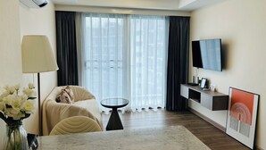 Ein modernes Hotelzimmer mit Bett, Fernseher, einem kleinen Tisch und einem großen Fenster mit Vorhängen.