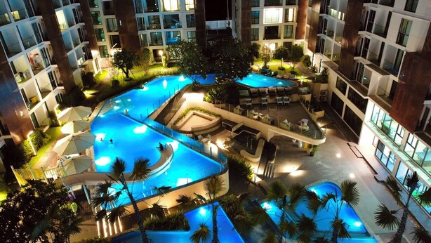Ein Mehrstöckiges Hotel mit großzügiger, überdachter Poolanlage, mehreren Balkonen und üppiger Bepflanzung.