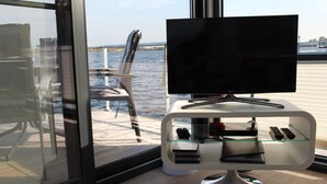 Une chambre moderne dotée d’une grande fenêtre, d’un téléviseur à écran plat posé sur une table en verre, et offrant une vue sur l’eau.
