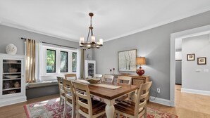Un comedor con una mesa de madera, sillas, una lámpara de araña, una ventana con cortinas, una lámpara y una alfombra.