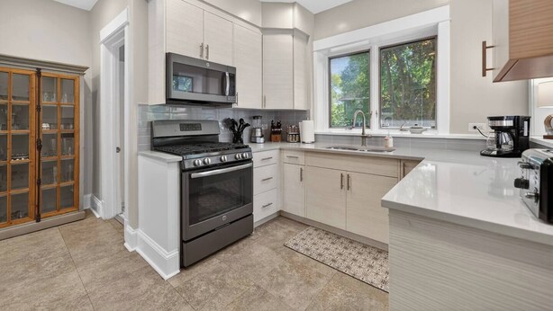 Una cocina moderna con armarios blancos, microondas integrado, estufa y cafetera.