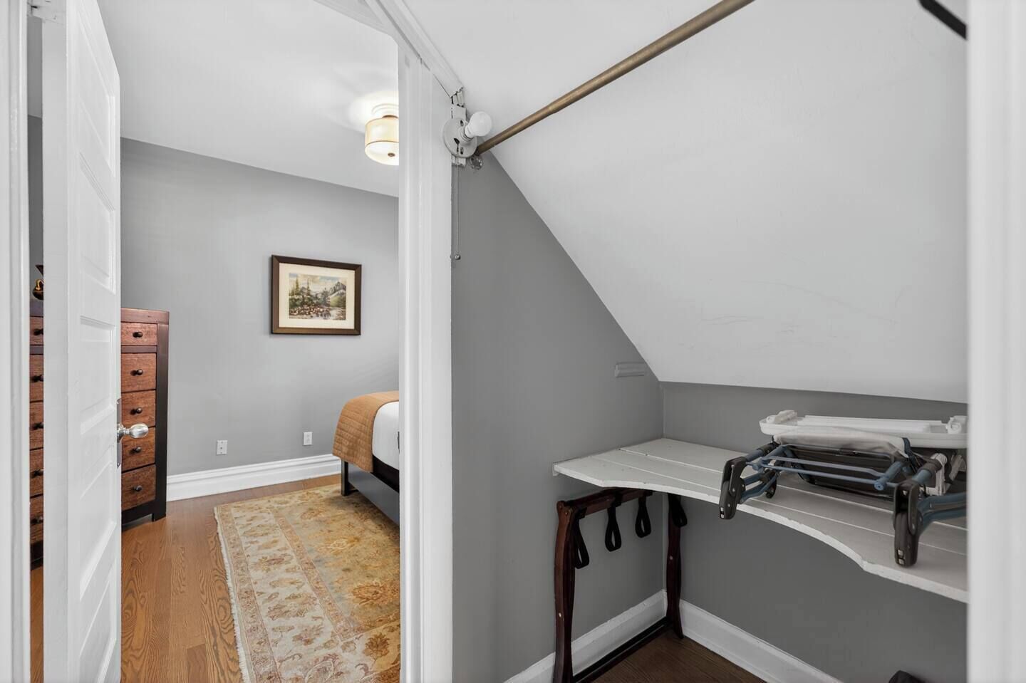 A bedroom with a sloped ceiling, a bed, a dresser, a framed picture on the wall, and a small table with a towel rack.