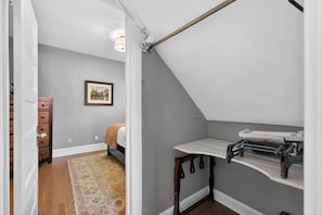 A bedroom with a sloped ceiling, a bed, a dresser, a framed picture on the wall, and a small table with a towel rack.