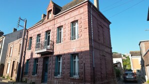 Un bâtiment en briques rouges, doté d’un balcon et de volets verts, situé dans une rue étroite.