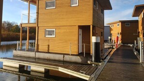A wooden cabin with a dock extending into a body of water, featuring a simple, modern design with two windows and a door. - Hausboot in Kroeslin am Bodden (Kröslin)