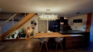 A modern kitchen with a wooden island, a dining area with two patterned chairs, and a staircase with wooden railings. - Just 15 minutes from the 24 Hours of Le Mans racetrack! Ideal for 10 people (Pruillé-le-Chétif)
