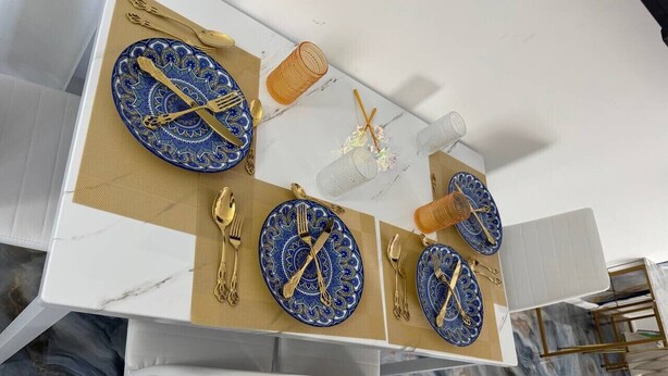 A dining area with a white table set with blue and gold plates, cutlery, and a woven napkin.