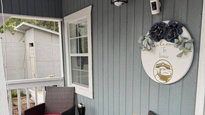 A covered porch with two wicker chairs with red cushions, a wall-mounted light fixture, and a welcome sign with a boat illustration.