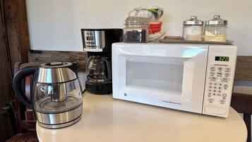 En köksbänk med en kaffebryggare, en mikrovågsugn och en glaskanna.