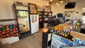 A store interior with a refrigerated display, shelves stocked with various items, and a table with colorful objects. - Short Branch Motel (Pahrump)