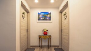 Un pasillo con suelo de madera, una mesa central con un jarrón de flores y un cuadro en la pared.