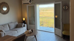 Una sala de estar con un sofá, una mesa de centro y una silla. Hay un balcón con vistas al campo.