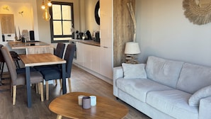 Una sala moderna con sofá, mesa de centro y comedor con sillas, con una cocina al fondo.