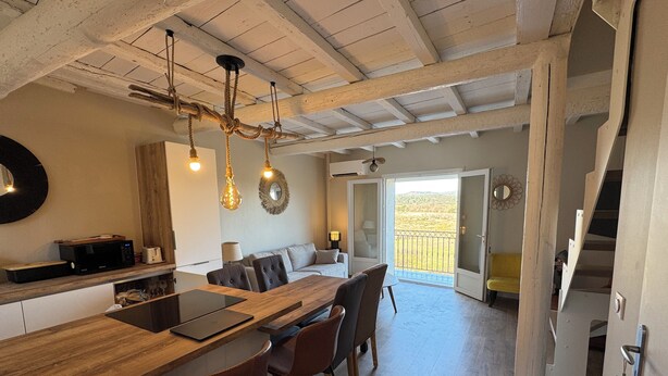 Cocina moderna con encimera de madera, taburetes de bar y una mesa de comedor. Se aprecia una vista a un balcón con barandilla.