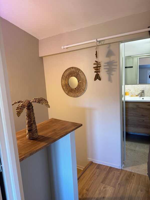 A hallway with a wooden shelf, a woven wall decoration, and a mirror.