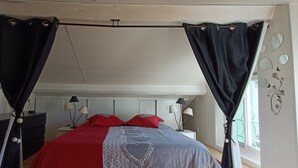 Ein Schlafzimmer mit einem Himmelsbett, zwei Nachttischlampen, einer Kommode und einem Fenster mit Vorhängen.