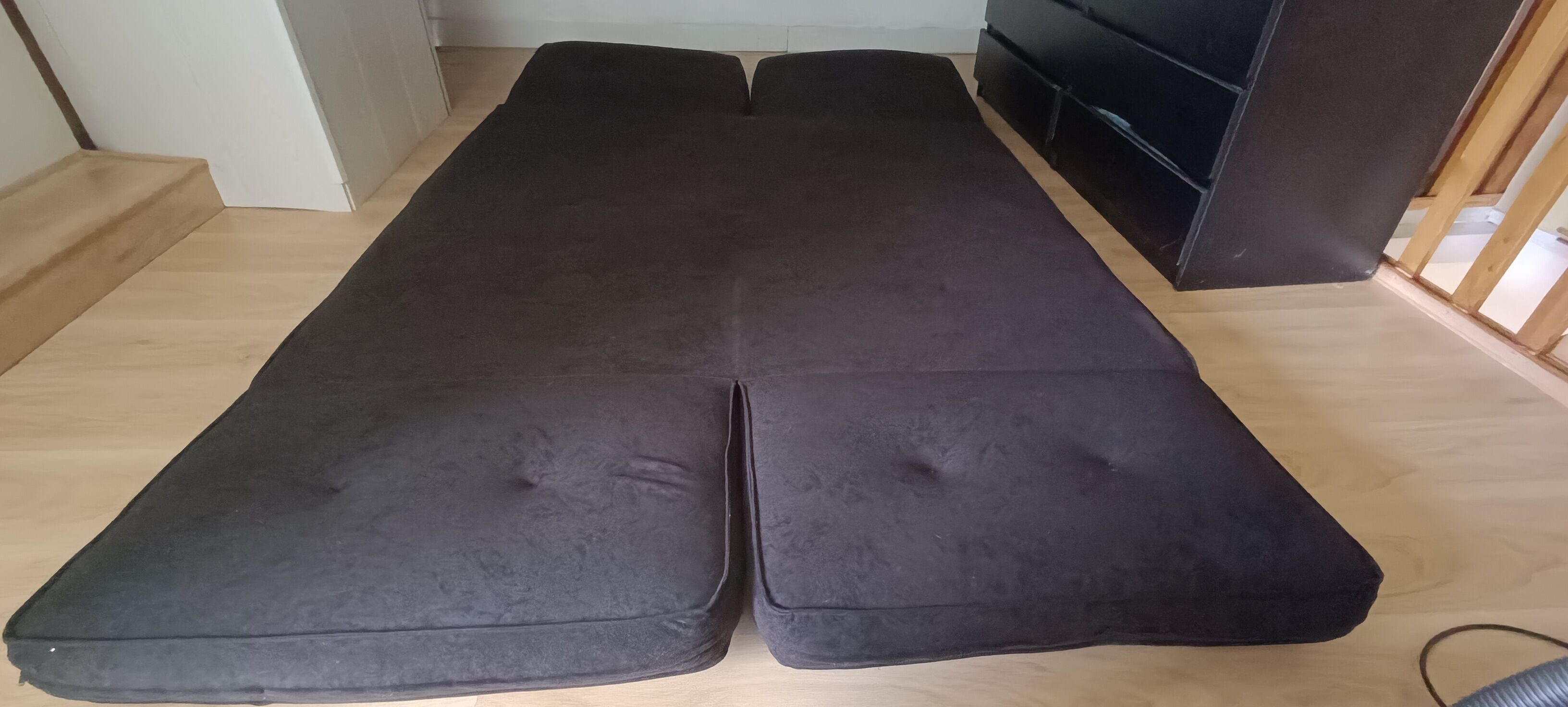 Una habitación con sofá negro y suelo de madera.