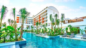 Un hotel con una piscina grande rodeada de palmeras y sillas de descanso.