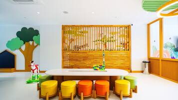 Un área de juegos para niños con una mesa grande, taburetes coloridos y una valla decorativa de madera con ilustraciones de animales.