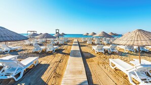 A beach with a wooden walkway leading to the sea, surrounded by white lounge chairs and thatched umbrellas. - Sy Hotels Belek - All inclusive (Serik)