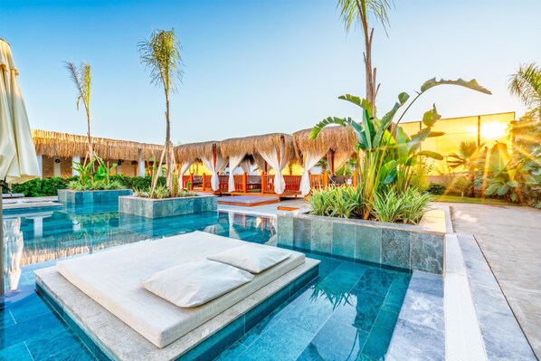 A swimming pool with a lounge area, thatched-roof structures, and tropical plants. - Sy Hotels Belek - All inclusive (Serik)