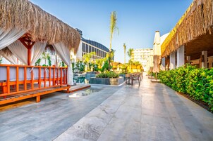 Un patio de resort con estructuras de techo de paja, piscina y zonas de estar al aire libre.