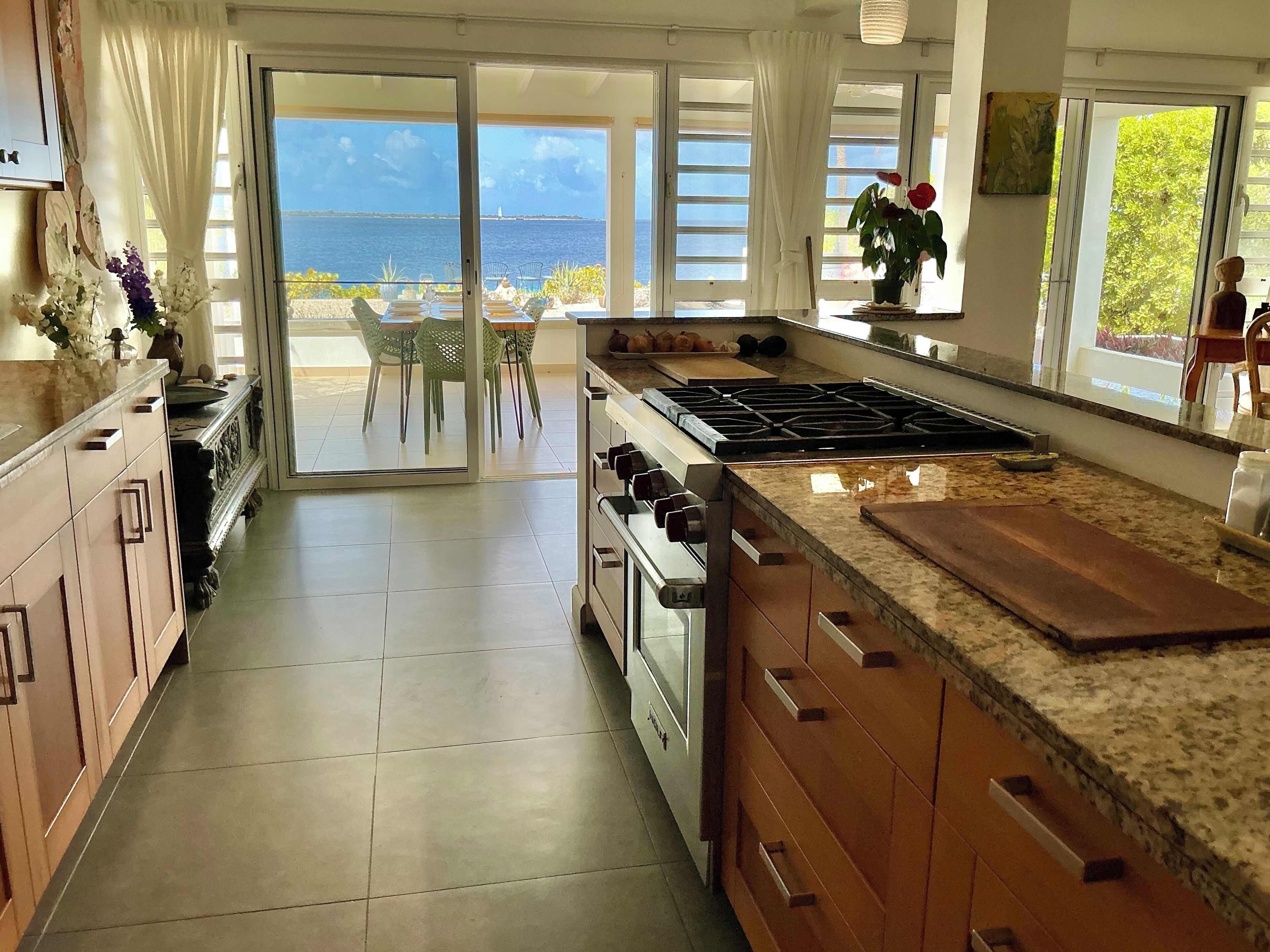 A kitchen with a large island, a stove, and a view of the sea through the sliding glass doors.
