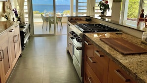 A kitchen with a large island, a stove, and a view of the sea through the sliding glass doors. - Beautiful oceanfront villa with beach and great house reef (Hato)