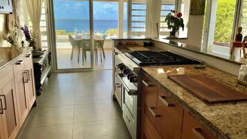 A kitchen with a large island, a stove, and a view of the sea through the sliding glass doors.