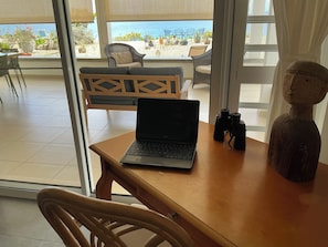Un ordinateur portable est posé sur une table en bois, avec vue sur la plage et sur les chaises qui se trouvent à l’extérieur.