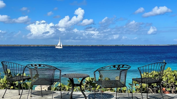 A seaside patio with three metal chairs and a small table, overlooking a clear blue sea with a sailboat in the distance. - Beautiful oceanfront villa with beach and great house reef (Hato)