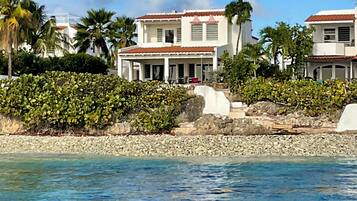 A beachfront property with a two-story building, a covered patio, and a rocky shoreline.