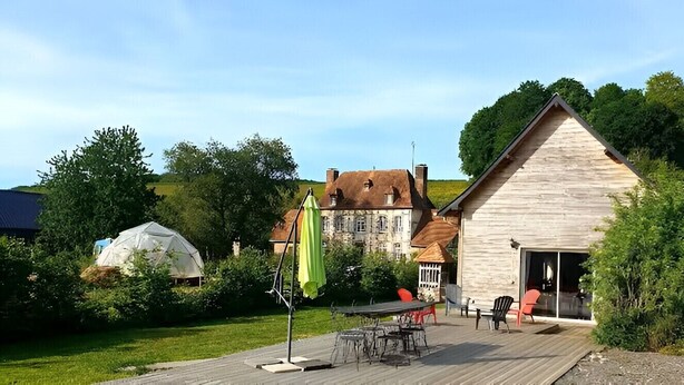 A wooden deck with outdoor furniture, a large umbrella, and a building with a sloped roof. - Detached house in the countryside adapted for disabled people Pets welcome (Osmoy-Saint-Valery)