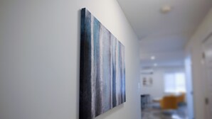 A hallway with a large abstract painting on the wall, leading to a room with a sofa and a window.