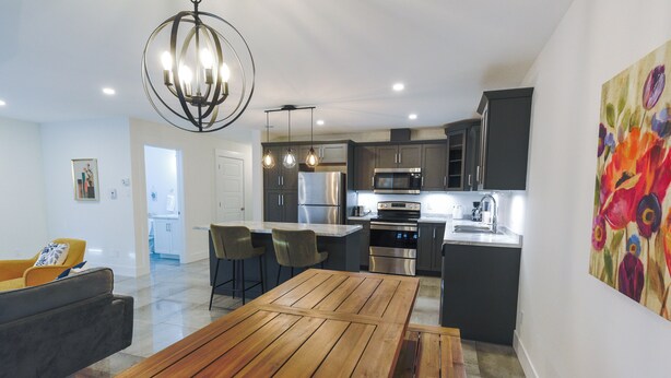 A modern kitchen with stainless steel appliances, a wooden dining table, and a pendant light.