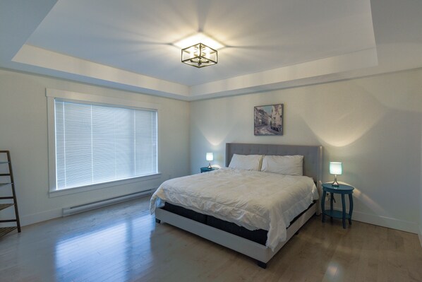 Une chambre à coucher avec un lit, deux tables de chevet avec des lampes, une fenêtre avec des stores et un tableau au mur.