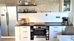 Una cucina moderna con un frigorifero in acciaio inossidabile, un forno Bosch e una macchina da caffè. Si notano mensole in legno sopra il bancone e un armadietto bianco con sportello in vetro.