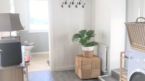 Una lavanderia moderna con lavatrice, stendibiancheria e cesto in vimini su uno sgabello di legno.