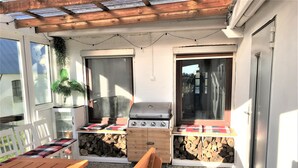 Un'area patio con tavolo in legno, sedie, barbecue e un piccolo giardino.