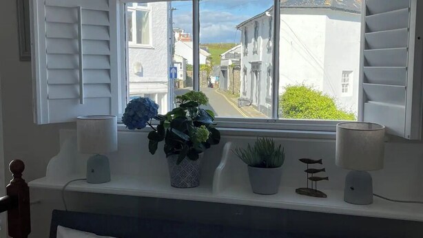 A bedroom with a large window, a bedside table with a lamp, a plant, and a small fish decoration. - Ringmore Cottage - Salcombe - View over estuary (Salcombe)