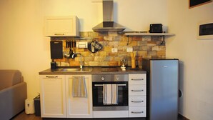 Una cucina compatta con forno integrato, frigorifero in acciaio inossidabile e zoccolo di pietra.