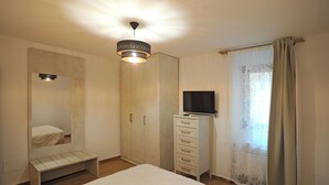 Camera da letto con un letto, un armadio, una televisione su un mobile e una finestra con tende.