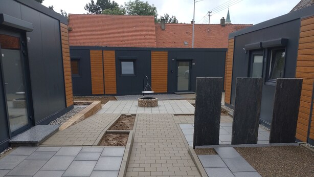 Een binnenplaats met een geplaveid pad, een kleine tuin en moderne gebouwen met grote ramen en houten details.