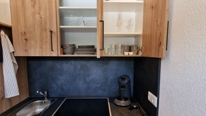 Een compacte keuken met houten kastjes, een zwart aanrecht, een roestvrijstalen spoelbak en een koffiezetapparaat.