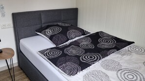 Een moderne slaapkamer met een grijs gestoffeerd hoofdeinde, een grijze bank en een bed met zwart-wit beddengoed.