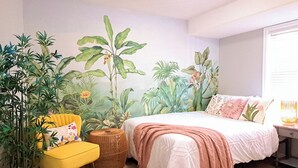 A bedroom with a bed, a yellow armchair, and a large plant.