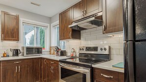 A modern kitchen with wooden cabinets, a stainless steel refrigerator, a microwave, a stove, and a window with blinds.