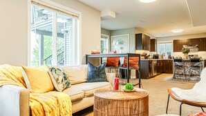 A spacious living room with a sofa, a round wicker coffee table, and a dining area with a kitchen in the background.