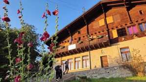 A rustic wooden building with a balcony, a stone wall, and a signboard. - La Cure de Vernamiège (Mont-Noble)